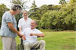 Happy man in a wheelchair laughing with his nurse and wife on sunny day in park