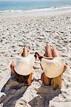 Sexy blonde and brunette in bikinis clinking their glass bottles on the beach