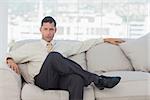 Serious businessman posing sitting on sofa in bright office