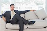 Serious businessman in suit posing sitting on sofa in bright office