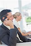 Cheerful businessman on the phone with his colleague working on computer in bright office