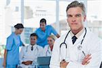 Experienced doctor posing with colleagues in background in medical office