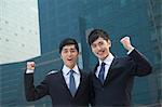 Two young businessmen outside glass building, smiling, portrait