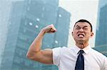 Portrait of young angry businessman flexing muscles