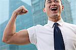 Portrait of young businessman flexing muscle outdoors