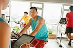 Young man on stationary bike exercising with his personal trainer