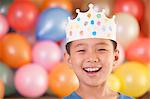 Birthday Boy Wearing a Crown in Front of Balloons