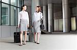 Two young businesswomen walking with suitcases and talking