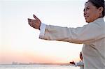 Two older people practicing Taijiquan on the beach at sunset, China