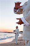 Two older people practicing Taijiquan on the beach at sunset, close up on hands