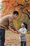 Father and daughter holding hands, looking at each other in the park, autumn