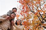 Family walking through the park in the autumn, little boy sitting on his fathers shoulders