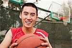 Young man sitting with a basketball on the basketball court, portrait