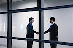 Two businessmen shaking hands, seen through glass wall