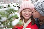 Young man kissing young woman in park in snow