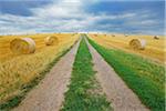 Field road through stubble field with straw rolls and rain clouds, Hesse, Germany, Europe