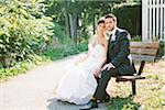 Portrait of Bride and Groom sitting on wooden bench outdoors, looking at camera, Ontario, Canada