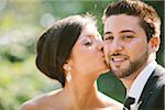 Close-up, outdoor portrait of Bride kissing Groom on cheek