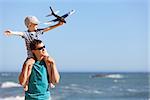 happy adorable boy holding toy plane and sitting on his young handsome father shoulders and having fun together outdoors