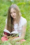 young girl reading book on field, vertical photo