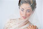 Portrait of beautiful happy bride posing with veil covering her face. Studio shot.
