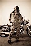 Photo of a beautiful female mechanic wearing overalls and standing in front of a motorcycle.