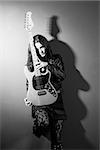 Photo of a female guitarist leaning up against a wall holding an electric guitar.