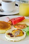 full meal for breakfast  ( pancake , fried egg , ham and sausage , fresh vegetable and fruits , hot coffee and juice )