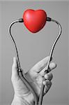 Man's hand holding a red heart and stethoscope