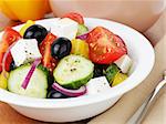 fresh greek salad in white bowl, on wood table