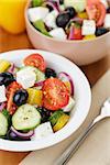 fresh greek salad in white bowl, on wood table