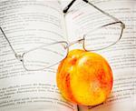 Pair of reading glasses on a dictionary toghether with a nectarine