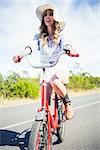 Cheerful trendy woman posing while riding bike in summertime on a road