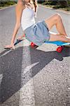 Body of young woman sitting on her skateboard on a deserted road