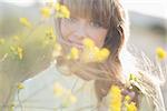 Hipster girl smiling at camera from behind yellow flowers in the sunlight