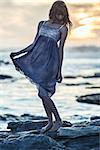 Beautiful young woman standing on rocks by the sea on a glowing background