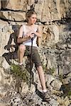 Blonde woman holding hiking pole looking away by a large rock face