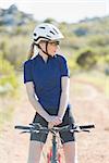 Woman with helmet sitting on bike and looking away in the countryside