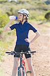 Woman with bike drinking water after biking in the countryside