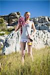 Smiling woman holding climbing equipment and looking up against rock