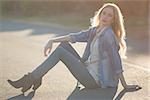 Fashionable woman sitting on road and posing in the sunshine