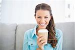 Portrait of attractive smiling woman holding cup of coffee sitting on cosy sofa