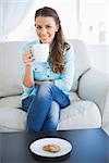 Young woman with coffee cup sitting on couch in bright living room