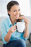 Smiling woman eating cookie holding cup of coffee looking at camera