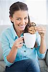 Smiling woman dunking cookie in coffee looking at camera