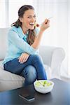 Smiling attractive woman eating healthy salad sitting on cosy sofa