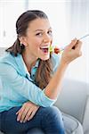 Cheerful attractive woman eating healthy salad sitting on cosy sofa