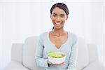 Smiling attractive woman sitting on cosy sofa in bright living room holding salad