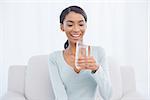 Smiling attractive woman sitting on cosy sofa in bright living room drinking water