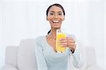 Smiling woman sitting on cosy sofa in bright living room holding glass of orange juice